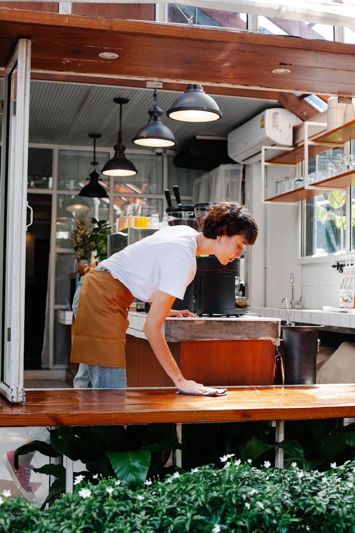 A barista wiping down a café counter, showcasing cleanliness and professionalism in a bright, airy setting.